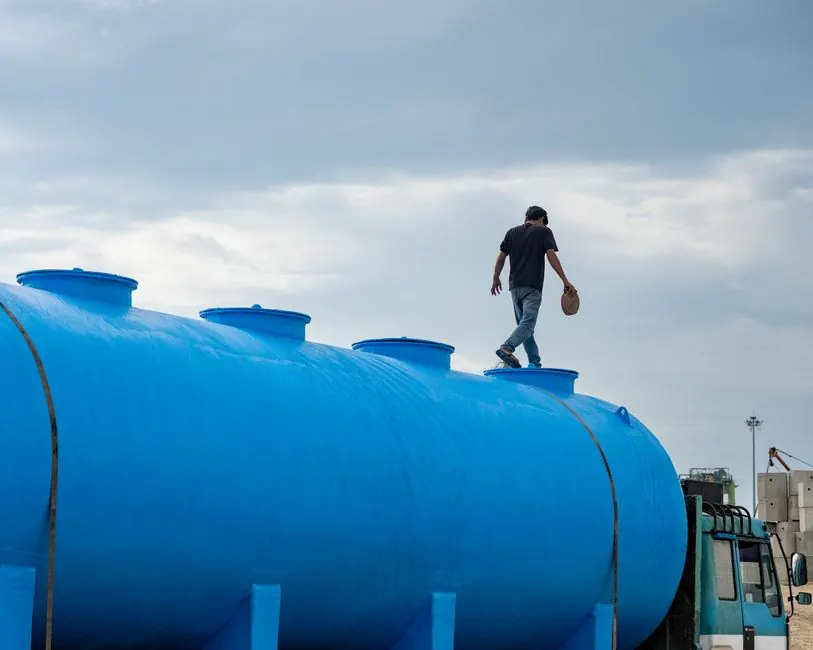 A person walking on a large blue water tank outdoors on a cloudy day.