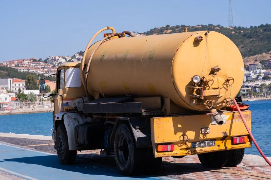Yellow water tanker truck parked by the blue seaside in Foça, İzmir, Türkiye.